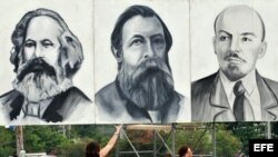 Dos turistas posan junto a carteles con los rostros de Marx, Engels y Lenin en la Plaza de la Revolución de La Habana.