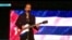 El artista cubano Willy Chirino cantando en un concierto con la bandera cubana detrás de él