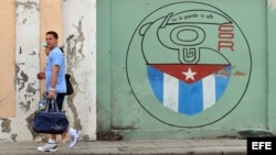 Una pareja camina junto a un cartel con el emblema de los Comités de Defensa de la Revolución en La Habana. 