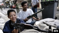 Archivo - Dos civiles permanecen atrincherados, ella con un fusil AKM y él con uno de utilería, en un n “enfrentamiento con el enemigo” en Centro Habana, el Día Nacional de la Defensa de Cuba. 