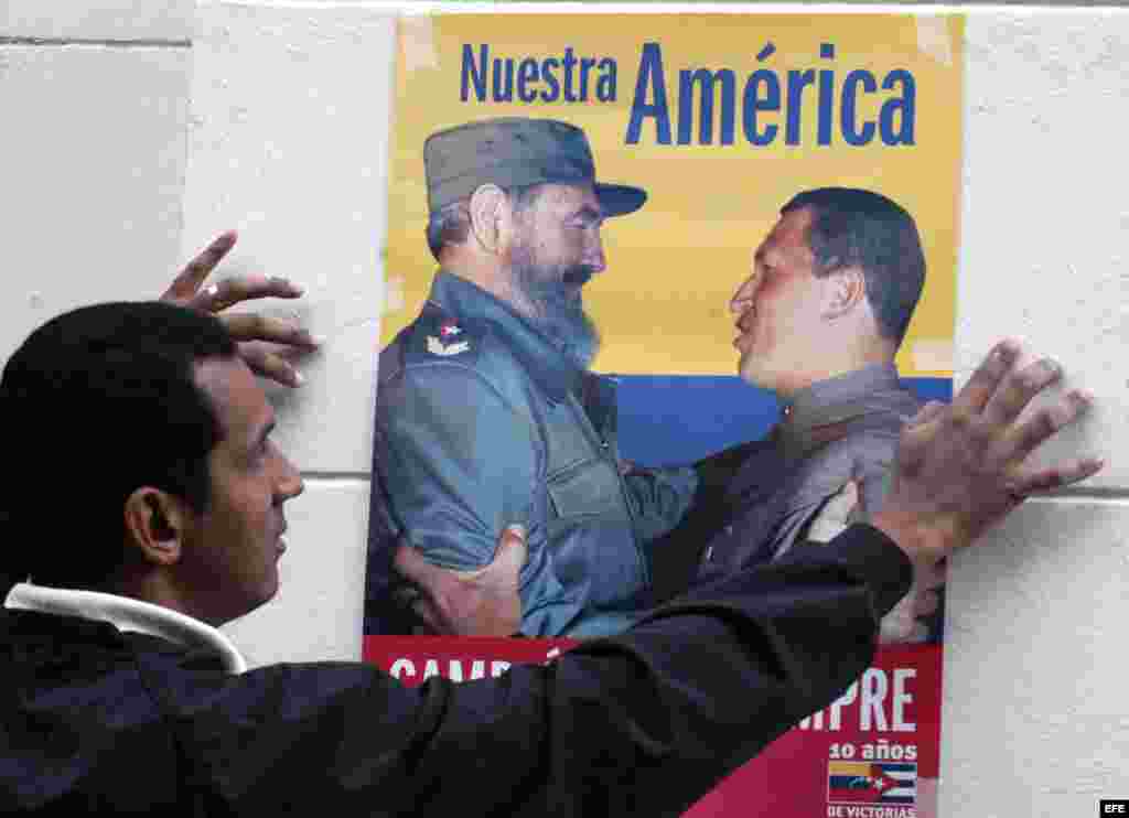 Una mujer barre la calle frente a un cartel del ALBA.