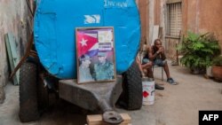 Un cubano descansa junto a un camión cisterna "pipa" donde han colocado un cartel con las figuras de Fidel y Raúl Castro el 9 de abril de 2018. 