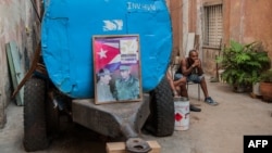 Un cubano descansa junto a un camión cisterna "pipa" donde han colocado un cartel con las figuras de Fidel y Raúl Castro el 9 de abril de 2018. (Archivo)