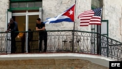 Dos jóvenes cubanos conversan junto a las banderas de Estados Unidos y Cuba.