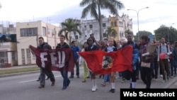 Adolescentes y jóvenes marchan por una calle de La Habana portando banderas de la UJC y la FEU.