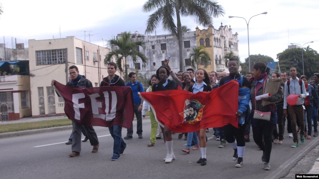 Adolescentes y jóvenes marchan por una calle de La Habana portando banderas de la UJC y la FEU.