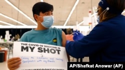 Un adolescente muestra un cartel de apoyo a la vacuna contra el COVID-19 mientras recibe su primera dosis de Pfizer. (AP /Shafkat Anowar, archivo)