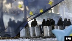 Varios policías antidisturbios montan un cordon policial tras una bandera de la Unión Europea cerca de una de las barricada un nuevo día de protestas contra el gobierno en el centro de Kiev (Ucrania).