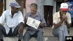 Un grupo de ancianos conversan sentados en un muro mientras esperan la llegada del periódico.