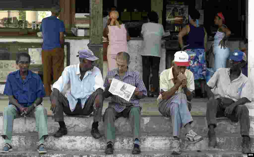 Un grupo de ancianos conversan sentados en un muro mientras esperan la llegada del periódico.