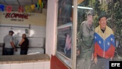 Dos hombres conversan en un establecimiento junto a un cartel de Hugo Chávez y Fidel Castro en La Habana (Cuba).
