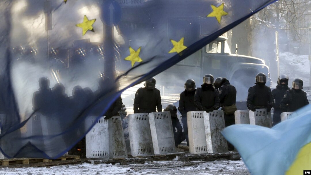 Varios policías antidisturbios montan un cordon policial tras una bandera de la Unión Europea cerca de una de las barricada un nuevo día de protestas contra el gobierno en el centro de Kiev (Ucrania).