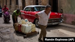 Cubanos trasladando envases de agua frente a un viejo auto estadounidense en La Habana. Foto AP/Ramón Espinosa. 