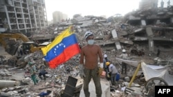Un rescatista voluntario se encuentra junto a una bandera venezolana sobre los escombros de un edificio colapsado en Caraballeda, estado de La Guaira, Venezuela, el 15 de julio de 2026, tras los terremotos gemelos del 24 de junio.