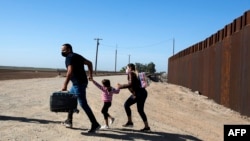 Una familia de migrantes de Cuba cruza corriendo la frontera por el muro que separa a Estados Unidos y México para entregarse a las autoridades el 13 de mayo de 2021 en Yuma, Arizona. (Foto de RINGO CHIU / AFP)