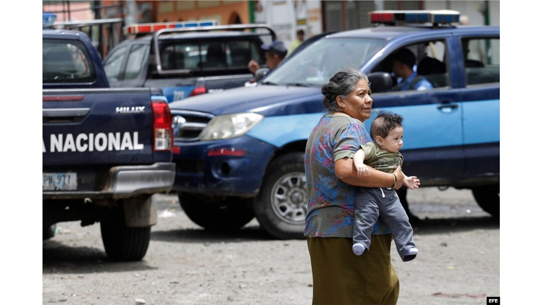 Una mujer carga a un bebé mientras la policía patrulla en Jinotega, escenario de la violencia en Nicaragua.