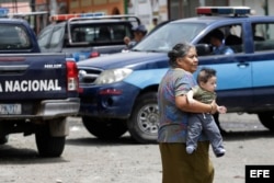 Una mujer carga a un bebé mientras la policía patrulla en Jinotega, escenario de la violencia en Nicaragua.