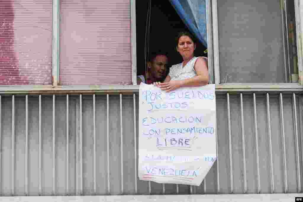 Una mujer sostiene un cartel desde su ventana al paso de estudiantes opositores al Gobierno y profesores universitarios que protestan en Caracas (Venezuela). 