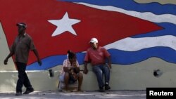 Un grupo de personas sentadas junto a un mural en La Habana.