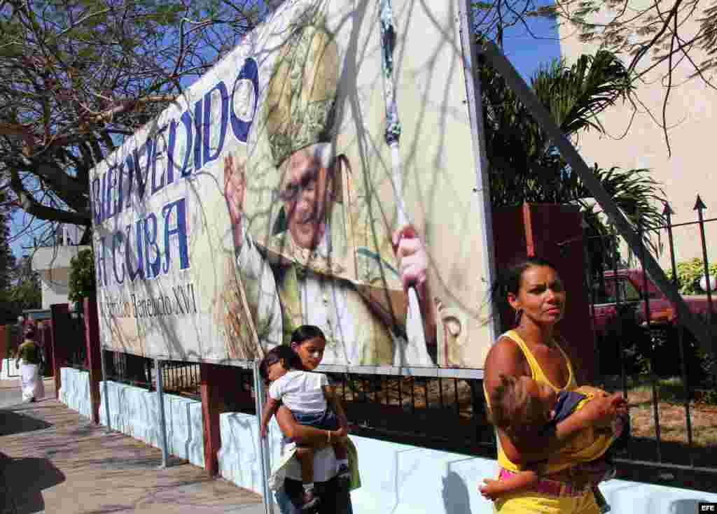 Dos mujeres caminan frente a una valla de bienvenida al Papa en La Habana, previo a la visita del Papa Benedicto XVI.