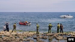 Guardafronteras observan a un grupo de cubanos a bordo de una embarcación rústica que intenta salir por mar hacia Estados Unidos.