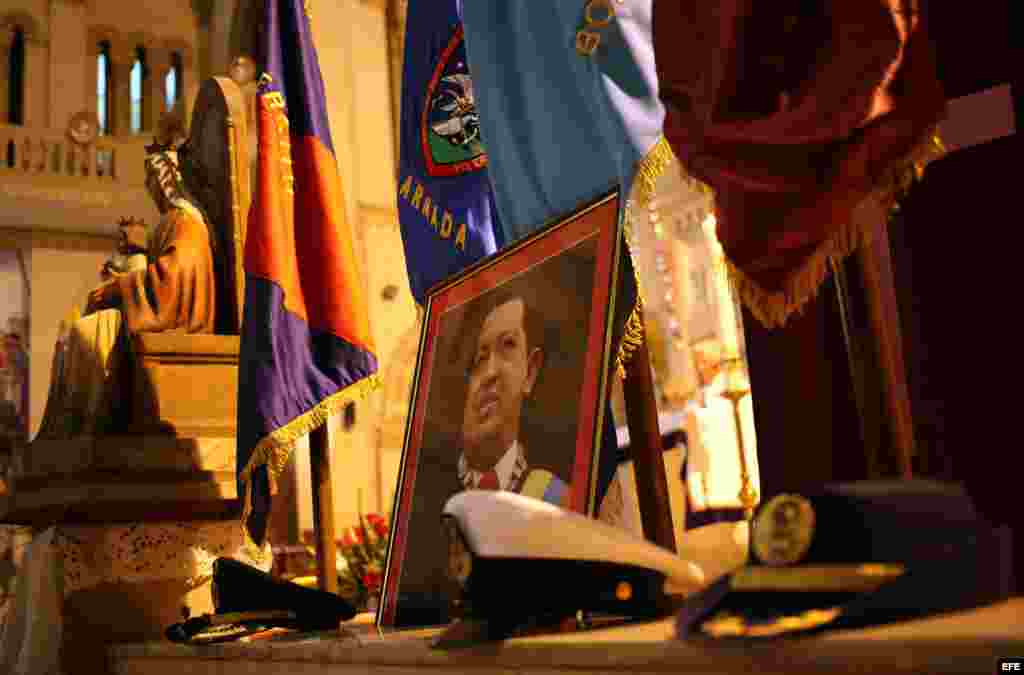 Vista de gorras militares colocadas a manera de ofrendas junto a un retrato del presidente de Venezuela, Hugo Chávez, en la iglesia Jesús de Miramar, en La Habana.