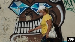 Mujer con máscara camina frente a mural alegórico a COVID-19 en Cuba