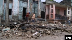 Dos hombres limpian escombros en una casa que ha sido parcialmente destruida por el paso del huracán "Sandy".