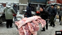 Un vendedor carga una carretilla con carne de cerdo para vender en un mercado de Shenyang, China.