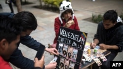 Una pareja de migrantes venezolanos pinta billetes en las calles de Bogotá para protestar contra la situación económica de su país. (Iván Valencia / AFP).