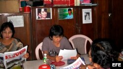 Archivo - Miembros de la Liga Nacional para la Democracia leen el periódico bajo un retrato de la líder opositora Aung San Suu Kyi en la sede del partido, en Rangún (Birmania).