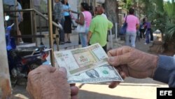 Un hombre muestra un peso convertible cubano y un dólar estadounidense frente a una oficina de la Western Union en La Habana.