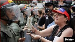 Una madre venezolana ofrece una estatuilla de la virgen a un efectivo de la Guardia Nacional Bolivariana. 