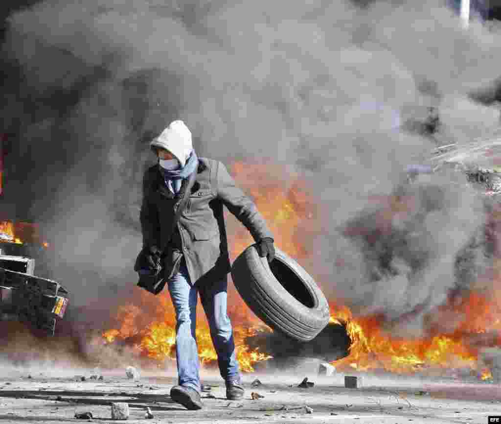 Un manifestante camina con un neumático durante los primeros choques entre opositores y policía después de varias semanas de tregua, en Kiev.