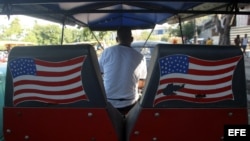 Un hombre conduce un bicitaxi en La Habana con banderas de Estados Unidos pintadas al fondo. EFE