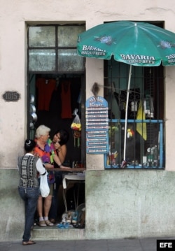 Tres mujeres conversan en la puerta de una vivienda donde se ha instalado un pequeño puesto privado de venta de artículos para el hogar.