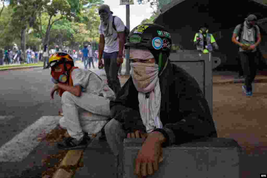 Manifestantes se protegen durante un enfrentamiento con policías antimotines hoy, jueves 4 de mayo de 2017, en Caracas (Venezuela). Los cuerpos de seguridad dispersaron con gases lacrimógenos la manifestación de estudiantes que se concentró en la Universi