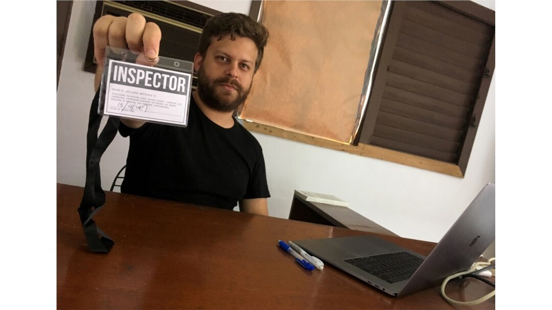 El artista cubano Leandro Feal sostiene una tarjeta de presentación que dice: "inspector", un performance que denuncia la figura de control artístico amparada bajo el Decreto Ley 349.