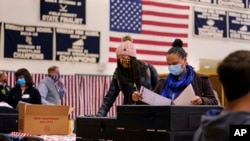 En esta fotografía de archivo del 3 de noviembre de 2020, dos mujeres, con máscaras protectoras debido al brote del virus COVID-19, emiten sus votos en un colegio electoral en la escuela secundaria Windham, Nueva Hampshire.