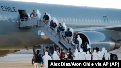 Migrantes venezolanos y colombianos que son deportados usan equipo de protección mientras caminan en línea con la policía para abordar un avión en el Aeropuerto Internacional General Diego Aracena Aguilar en Iquique, el 10 de febrero de 2021.