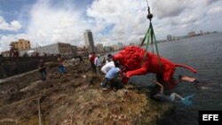 El artista plástico cubano Roberto Favelo (i) posa junto a un león rojo creado por él que conforma la obra "Garras en la piedra" que se instala en los arrecifes del malecón de La Habana (Cuba). Esta pieza forma parte de la exposición colectiva "Detrás de