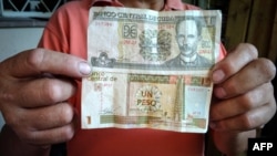 Un trabajador muestra un peso cubano (CUP) y un 1 CUC, que según la tasa oficial de cambio equivale a 25 CUP.