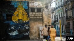 Cubanos en un área restrigida por casos de COVID-19, junto a una imagen de la Virgen de la Caridad. (YAMIL LAGE / AFP)