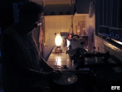 Una mujer lava los platos iluminada por una lámpara de queroseno durante un apagón