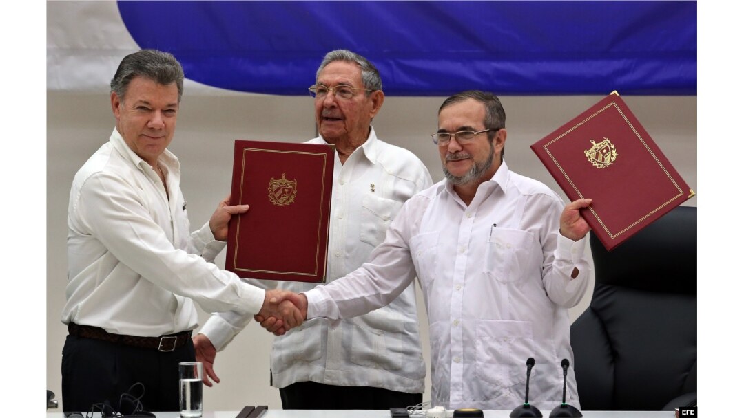 El delegado de las FARC en Cuba, Rodrigo Londoño Echeverri, alias "Timochenko" (d) y el presidente de Colombia, Juan Manuel Santos (i) junto a el presidente de Cuba, Raúl Castro (c) sostienen en sus manos el acuerdo de paz.