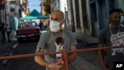 Hombres montan guardia en una reja que corta el acceso a su vecindario en cuarentena por coronavirus, en La Habana, para mantener alejados a los que no viven allí. (AP/Ramon Espinosa)