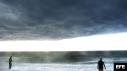 Dos hombres observan las fuertes olas y el cielo nublado en una playa del oeste de La Habana. Archivo.
