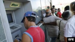 Un residente local extrae dinero de un cajero automático mientras otros hacen fila.