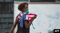 Una mujer con una máscara protectora contra el coronavirus y una bandera de EEUU camina por una calle de La Habana. (Yamil Lage/AFP)