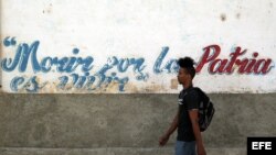 Un joven camina junto a un muro con un frangmento del himno nacional de Cuba. 